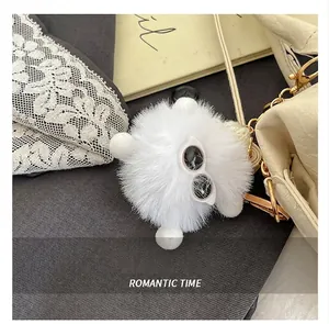 Detail of a white fuzzy charm with sunglasses and golden hardware on a shoulder bag