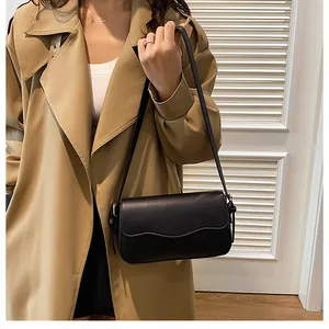 Détail du sac à bandoulière noir au bord ondulé porté par un mannequin en trench-coat