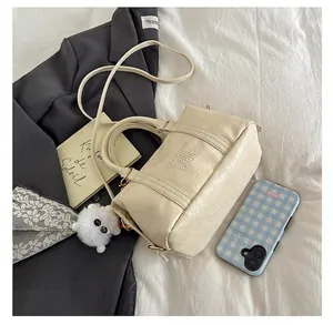 Chic beige textured Boston bag with plush charm on a cozy lifestyle bed setting