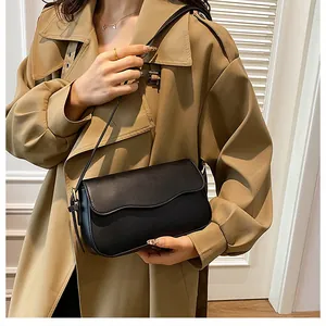 Détail d'un sac bandoulière noir en cuir minimaliste avec rabat ondulé sur un trench-coat