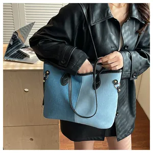 Detail of denim patchwork tote bag with black leather handles and gold metal hardware
