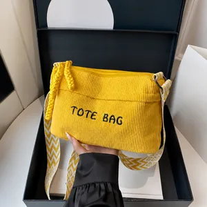 Primer plano del bolso tote de pana amarilla con bordado y correa geométrica en caja regalo