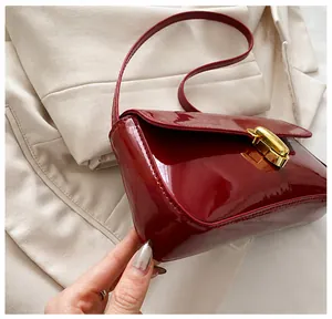 Side view of wine red patent leather underarm bag with gold metal buckle and glossy finish