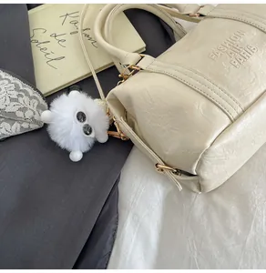Detail der cremefarbenen Boston Bag mit Logo-Prägung und Plüsch-Anhänger im Vintage-Look