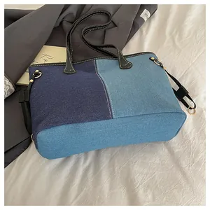 Detail view of patchwork denim tote bag with blue panels and black leather straps