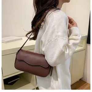 Vue détaillée du sac bandoulière marron foncé avec rabat ondulé sur un pull en maille blanc