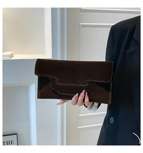 Detail of dark brown suede envelope clutch bag held against a minimal background