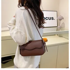 Détail du sac à bandoulière marron foncé avec rabat ondulé et pompon en cuir élégant