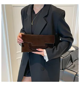 Detailed close-up of dark brown suede envelope clutch with geometric flap held by a model