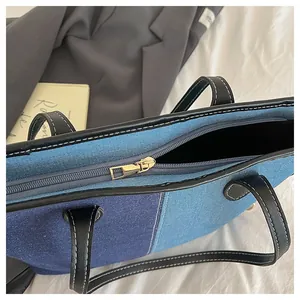Detail of denim patchwork tote bag with gold zipper and black leather handles