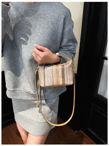 Detail of striped woven straw handbag featuring tan leather trim and adjustable shoulder strap