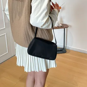 Minimalist black nylon underarm bag with zipper closure shown on shoulder of a model
