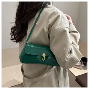 Detalle de bolso baguette de charol verde con cierre en J dorado sobre gabardina beige
