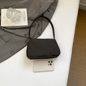 Minimalist black shoulder bag with metal zipper shown next to a smartphone for size scale