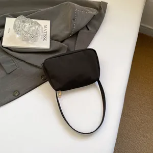 Close-up of black nylon shoulder bag with gold zipper next to a grey blazer and art books