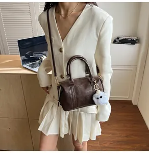 Detailansicht einer dunkelbraunen Boston-Tasche mit Plüschanhänger und goldenen Beschlägen