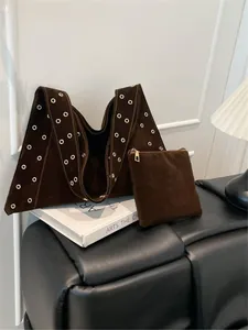 Détail du sac cabas en daim marron avec œillets métalliques dorés et sa pochette assortie