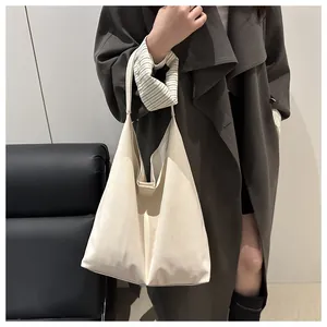 Detail view of a large cream tote bag with wide shoulder strap shown on model's shoulder