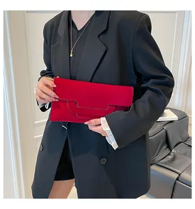 Minimalist red suede envelope clutch with geometric layered design held against a black suit