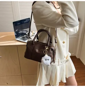 Detail der dunkelbraunen Boston-Tasche aus Leder mit weißem Plüschmonster-Anhänger