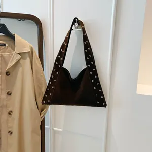 Détail d'un sac à bandoulière en daim marron foncé avec œillets métalliques argentés