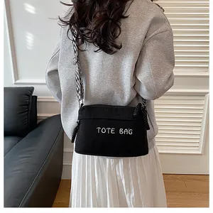 Detail of black corduroy crossbody bag featuring white TOTE BAG embroidery and wide strap