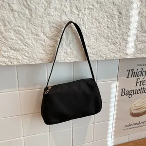 Minimalist black nylon underarm bag with gold zipper detail against a French aesthetic wall
