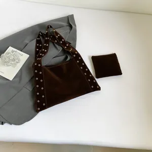 Détail du cabas en daim marron foncé avec œillets dorés et petite pochette assortie
