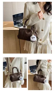 Detailansicht der braunen Boston-Tasche aus Leder mit Logo und flauschigem Anhänger