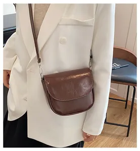 Detail of a glossy brown saddle crossbody bag with silver hardware on a white blazer