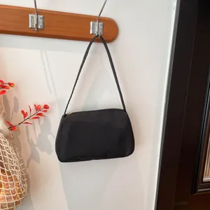 Minimalist black rectangle shoulder bag hanging on wooden hook with red leaves background