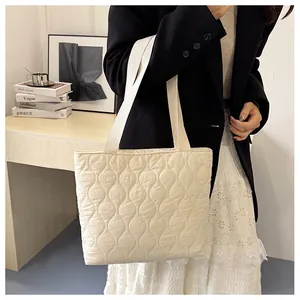 Detail of cream quilted tote bag featuring elegant wave stitching and woven straps