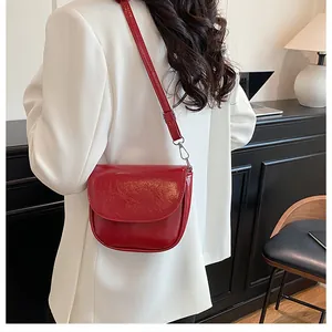 Detail of burgundy saddle bag in glossy leather worn with a white blazer for women
