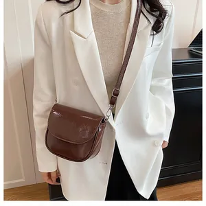 Detail of a deep coffee saddle bag in glossy patent leather worn over a white blazer