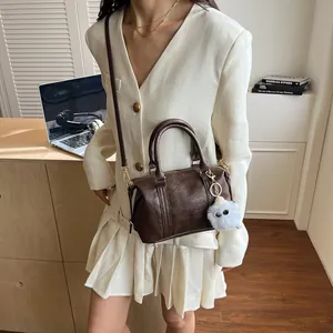 Dunkelbraune Boston-Tasche mit Schultergurt und Plüsch-Anhänger auf weißem Blazer
