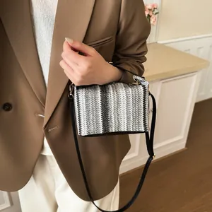Fashionable black and white woven crossbody bag with chain strap on a brown blazer model