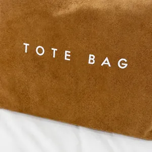 Vue détaillée du sac cabas en daim marron avec texture de qualité et logo blanc imprimé