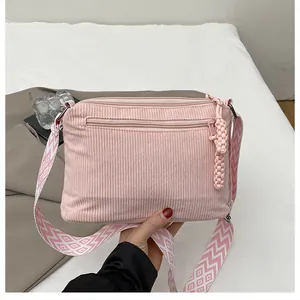 Detail der pinkfarbenen Cord-Umhängetasche mit gewebtem Anhänger und breitem Gurt