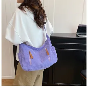 Detailed texture of purple corduroy crossbody bag with vertical zipper pockets shown on model