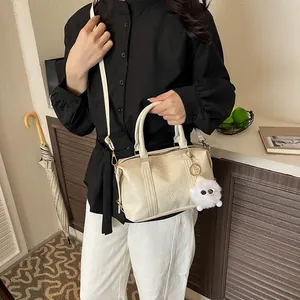 Schicke cremefarbene Boston-Handtasche mit Lederstruktur und Plüsch-Anhänger in Wohnambiente