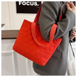 Detail of red quilted tote bag with wavy stitching and wide shoulder strap on model