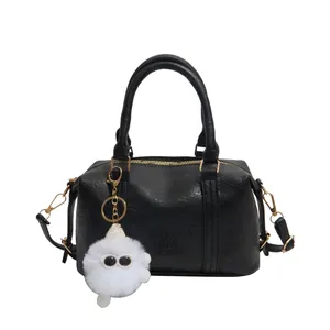 Klassische schwarze Boston Bag mit goldenen Details und einem weißen Plüsch-Anhänger