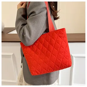 Close-up of red quilted puffer tote bag shown on model's shoulder for size perspective