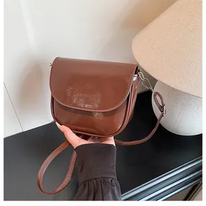 Detail of a dark brown glossy saddle bag with a subtle embossed logo and metal hardware