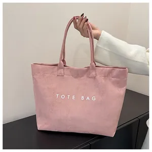 Detailed view of pink suede tote bag with white lettering and long shoulder straps