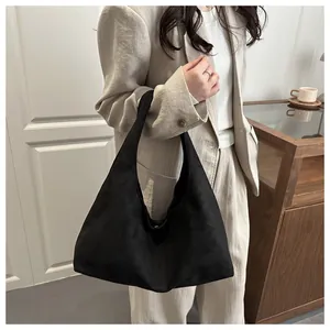 Détail d'un grand sac hobo noir en daim porté à l'épaule par un mannequin chic