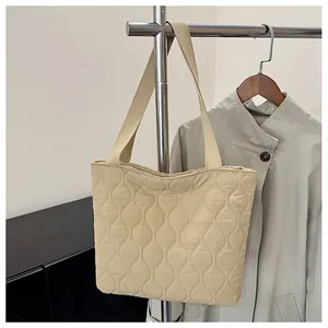 Detail of beige quilted shoulder bag with wave patterns hanging on a metal rack