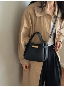 Detail of black lychee grain handbag featuring a golden swivel lock on a khaki trench coat