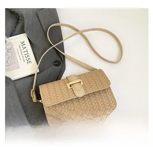 Detail van beige gevlochten baguette tas met gouden gesp op grijze blazer achtergrond