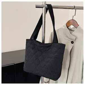 Detail of black quilted puffer tote bag showing curved diamond stitching and thick strap